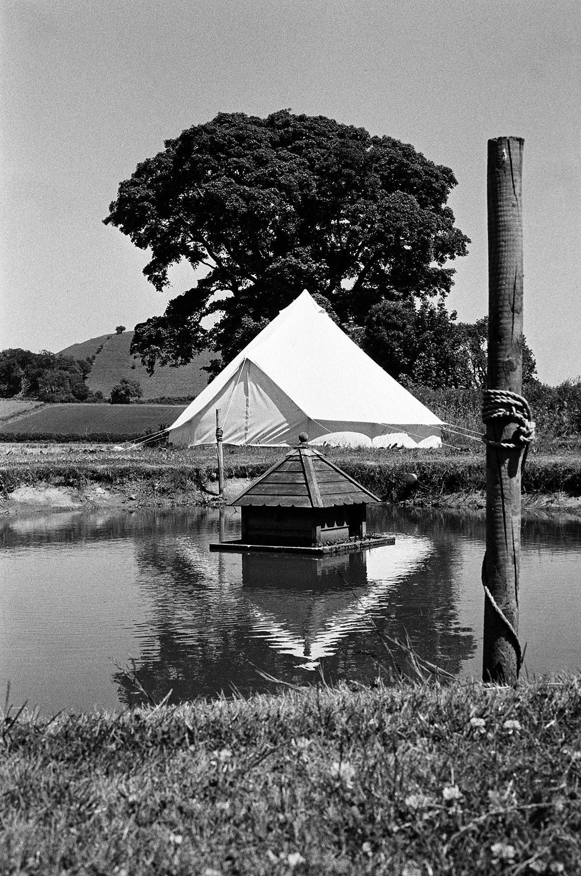 A bell tent and floating duck house on a pond