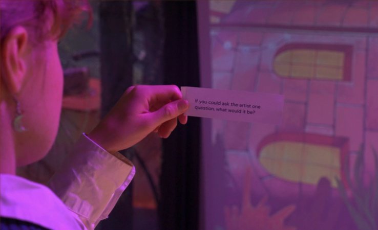 A visitor holding a prompt card up to a projected street art photo